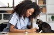 © Stavros - Female veterinarian with loose hair in medical gown carefully examines large cat in veterinary clinic office. Black woman vet doctor carefully examines adult cat sitting on table for health problems