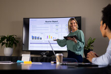 Happy Casual Businesswoman With Tablet Presenting At Screen To Diverse Female Colleague At Meeting