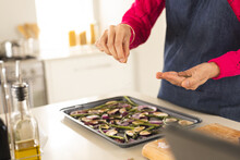 Hands Of Biracial Woman In Apron Seasoning Vegetables In Kitchen