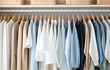 White, beige and blue clothes lay on shelves and hang on wooden hangers in a large white wooden closet