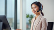 © KRISTINA KUPTSEVICH - Smiling young Asian woman operator working with headsets and desktop computer at telemarketing customer service, call center on office background. contact or talking with customer concept