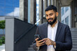 A young Muslim male businessman is using a mobile phone while standing outside an office center. Close-up photo
