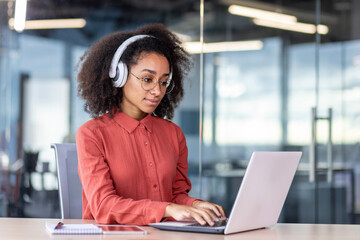 Serious concentrated woman working with laptop inside office, businesswoman thinking with headphones typing on keyboard, programmer developer listening to audio podcast, training course.