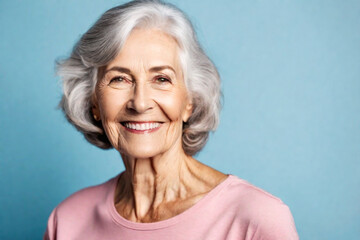 Wall Mural - Happy beautiful elderly senior model with grey hair in a pink t-shirt on a blue background, portrait of beauty mature old woman with hairstyle and makeup, healthy face skin with wrinkles, dental care