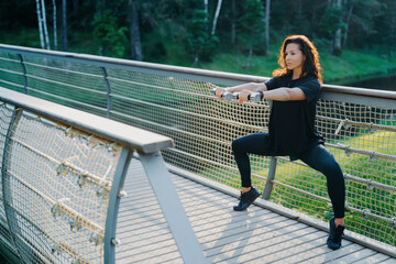 Wall Mural - Fitness-focused woman in black performing squats on a bridge amidst nature, showcasing strength and determination