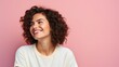 Close up studio shot of beautiful young mixed race woman model with curly dark hair looking aside with charming cute smile while posing against pink blank copy space wall for your content