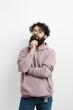 © arthurhidden - Pensive bearded man in glasses and a mauve hoodie, hand on chin, lost in thought against a clean white background