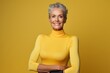 Portrait of a merry woman in her 60s showing off a lightweight base layer against a soft yellow background. AI Generation