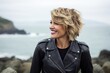 Portrait of a joyful woman in her 40s sporting a classic leather jacket against a serene seaside background. AI Generation