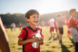 Happy kid drinks water after football game with teammates in the field