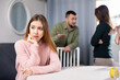 © JackF - Upset woman sitting at table while man and woman arguing behind her back