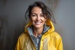 Portrait of a blissful woman in her 50s sporting a waterproof rain jacket against a bare concrete or plaster wall. AI Generation