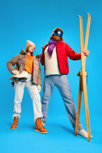 Funny Portrait Of Father And Daughter Dressed Winter Outfit, Warm Suit And Goggles Mask And Holds Vintage Ski And Skates Isolated Blue Studio Background.