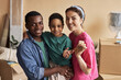 © Seventyfour - Young intercultural family of father, mother and cute son holding key to their new apartment while standing in front of camera and looking at you