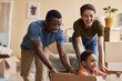 © Seventyfour - Happy young intercultural husband and wife pushing big cardboard box with their cute little son inside while playing during relocation
