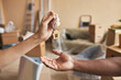 © Seventyfour - Hand of young female real estate agent passing keys to male owner of new apartment or house in front of camera against living room interior