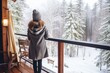 woman standing on balcony of wooden house at winter forest. Back view of female tourist in new cottage.