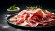 Prosciutto ham. Sliced Prosciutto with Rosemary on a dark background. Close-up of sliced of Parma ham on black plate with herbs. Cured meat delicacy with fresh herbs on dark Backdrop. Italian food