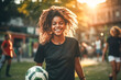 Young afro woman with her curly hair, soccer player, smiling and happy, holding soccer ball in park.