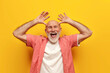 joyful old grandfather in summer shirt fooling around and making faces on yellow isolated background