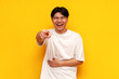 young asian guy in a white t-shirt laughs and points his hand forward on a yellow isolated background