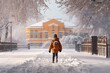boy in a warm orange jacket walking in the snow in front of the school. Back view