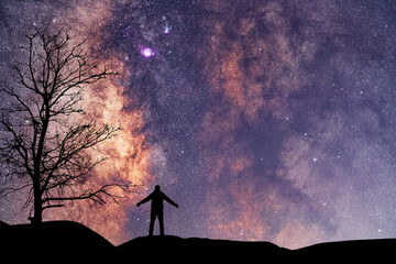Wall Mural - silhouette of a hiker standing on the hill, on the milky way galaxy background. cosmos wallpaper.