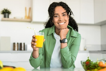 Wall Mural - black woman holds glass of orange juice in her kitchen