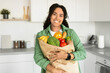 © Prostock-studio - African American woman hugs paper groceries shopping bag in kitchen