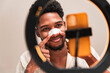 © ADDICTIVE STOCK - A cheerful young latin man applies a pore-cleansing nose strip while looking in the mirror, highlighting a personal grooming moment.