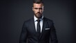 © OKAN - Stylish businessman in suit and tie against dark backdrop.