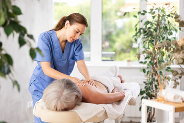 Wall Mural - Young female masseuse doing back massage to elderly woman client in massage room