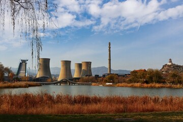 Old steel factory view with a chimney and cooling tower with lake near