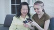 © anut21ng Stock - Elderly mother of Asian daughter using smartphone to shop online with credit card while sitting on the sofa at home