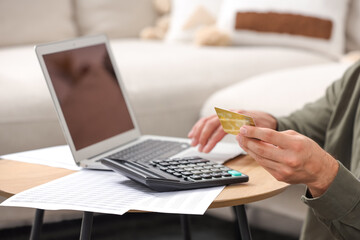 Canvas Print - Man with laptop, calculator and credit card planning budget at table indoors, closeup. Debt problem