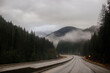 © Liudmila - Asphalt road in the middle of high mountains, covered with fog and clouds, at dusk. American winter landscape of a mountainous area covered with fir forest