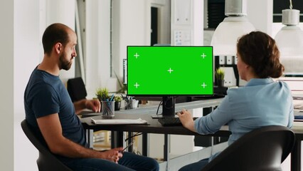 Corporate team using greenscreen on monitor while sitting at agency workstation, small business development. Man and woman colleagues looking at display showing isolated copyspace.