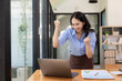 © ArLawKa - Happy, excited, success in business, Asian woman wins in office, beautiful Asian woman celebrates with laptop. happy success gesture ecommerce