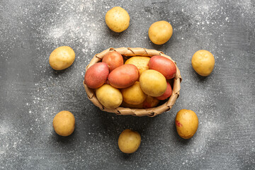 Wicker bowl with fresh raw potatoes on grey background