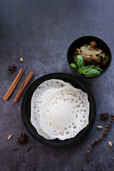 Poster - Appam, Kerala breakfast food duck curry or hot and spicy chickpea Masala and milk tea chai, Christian breakfast on dark black background. fermented rice pan cake. Top view of Indian veg food.