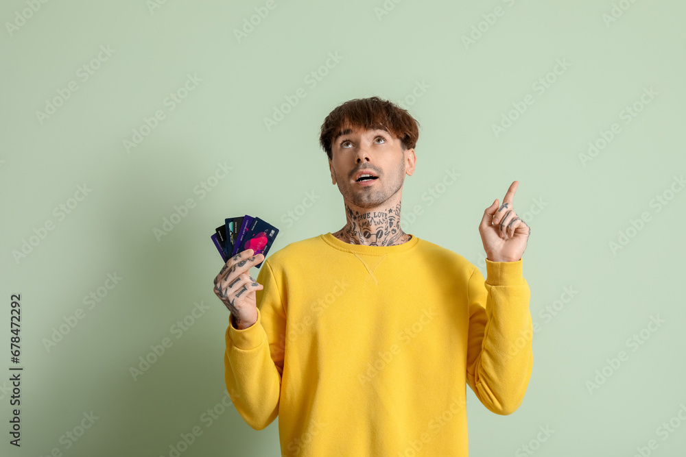 Tattooed young man with credit cards pointing at something on green background