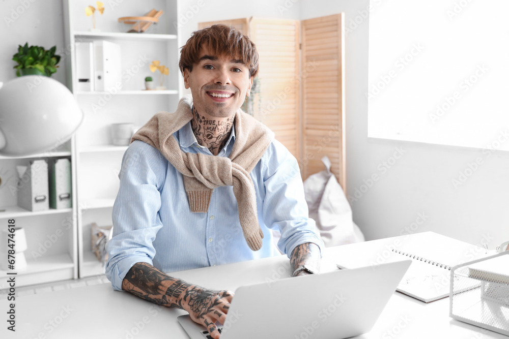 Handsome young tattooed businessman working with laptop at workplace in office