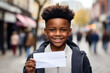 Joyful boy with a wide smile presenting a blank piece of paper in a town setting, his charisma perfect for engaging advertisements.
