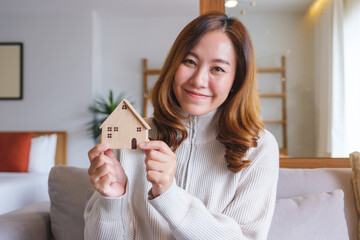 Wall Mural - Portrait image of a young woman holding and showing a wooden house model