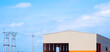 Industrial workshop building with electric poles and cable lines against blue sky background in panoramic view