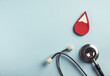 Red blood drop with medical stethoscope on pastel blue background. Iron deficiency anemia, hemophilia, blood donation concept. Top view, copy space