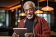 © Georgii - Cheerful senior grey-haired African American man in casual clothing uses digital tablet while sitting on sofa at home. Focused retired person browsing the Internet, watching news, reading e-book.
