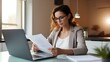 © yj - Focused female adviser holding financial reports and working online over laptop at desk in home office. Effective telecommuting concept. generative AI