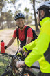 © Westend61 - Smiling man holding water bottle and talking to friend in forest