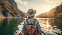 Rear view of young woman traveler with backpack on boat among mountains enjoying sunset